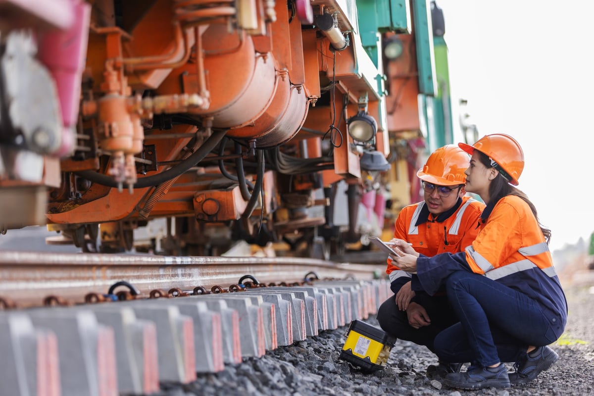 Two engineers in safety uniforms and helmets inspect mechanical equipment, discussing details to ensure precision and performance